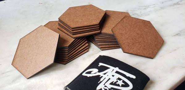 Stacks of blank hexagonal MDF coasters on a light work surface